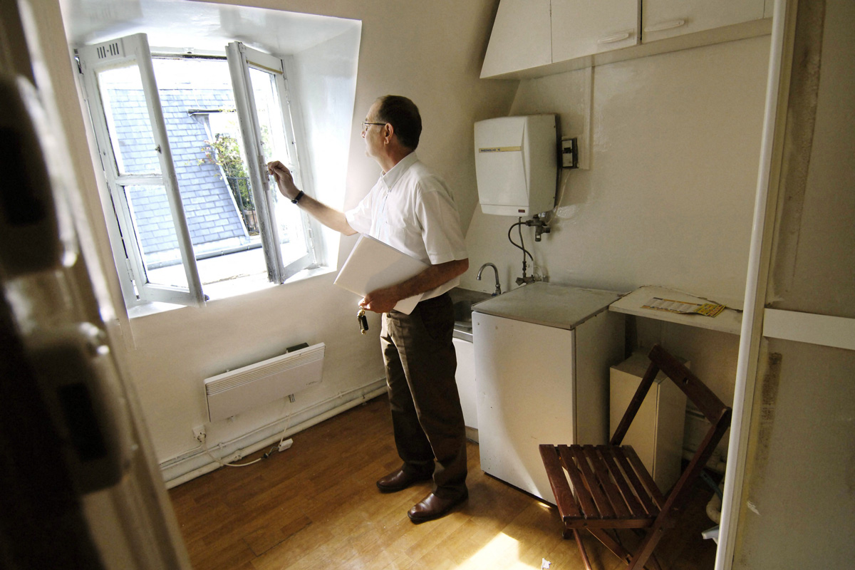 Un agent immobilier se tient debout et ouvre une fenêtre pour montrer la vue sur Paris depuis une chambre de bonne.