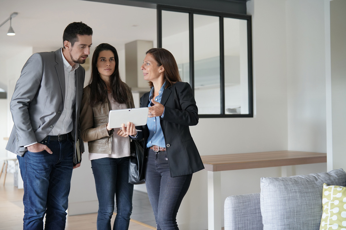 Un couple de trentenaires visite un appartement lumineux et moderne avec un agent immobilier.