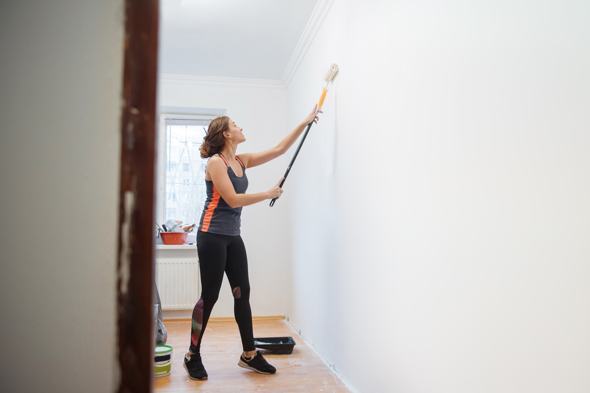 Une femme peint un mur blanc pour rénover son appartement