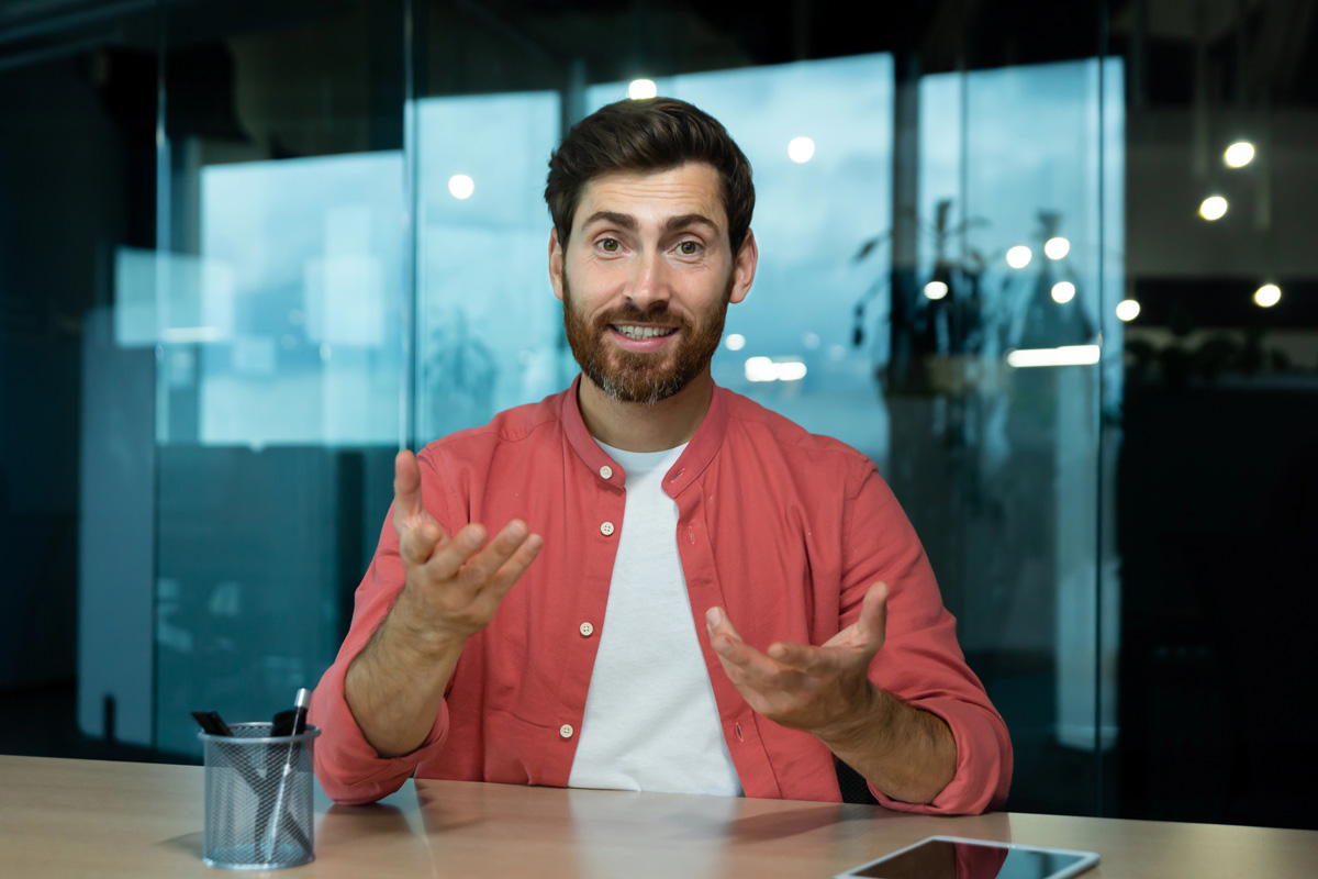 Un homme en chemise rouge parle face caméra dans des bureaux modernes en verre