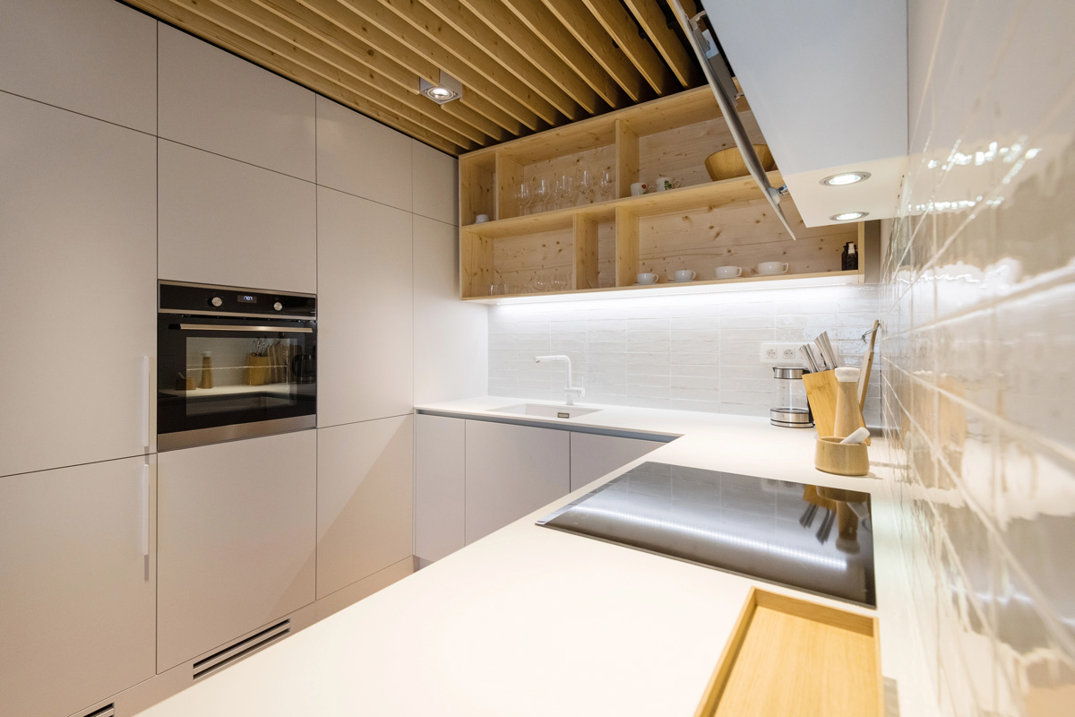Intérieur d’une cuisine moderne en bois brut clair et en faïence blanche, optimisée pour les équipements et les rangements dans un petit espace