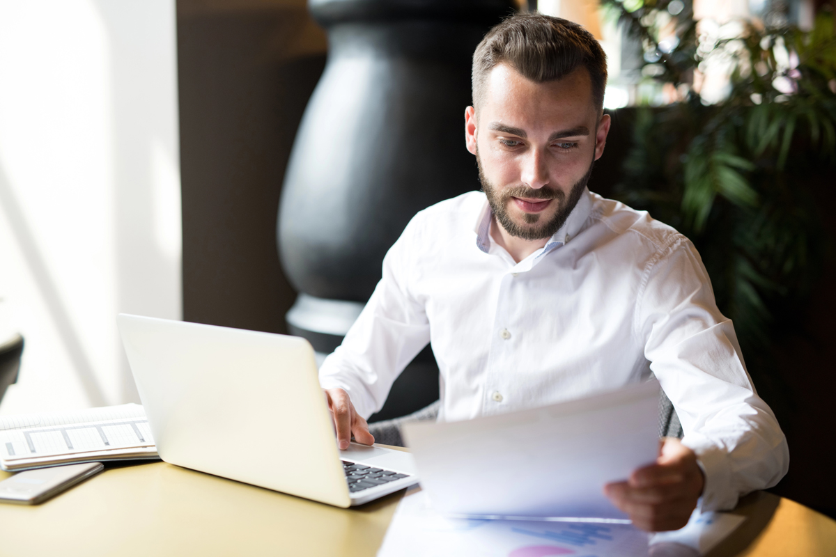 Un homme compare des documents sur son ordinateur avec des documents papier