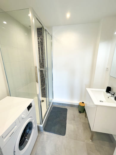 Salle de douche rénovée et optimisée avec douche, lavabo et machine à laver