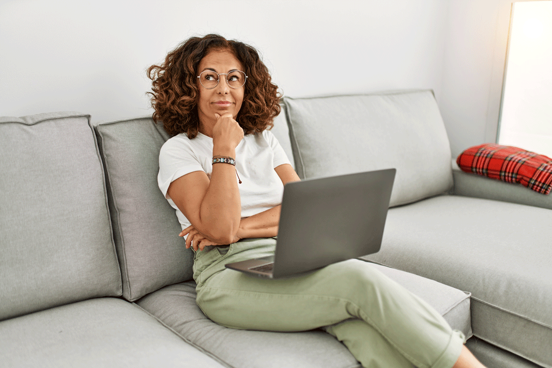 Une femme assise sur un canapé se demande s'il est intéressant d'investir en nom propre dans l'immobilier locatif.