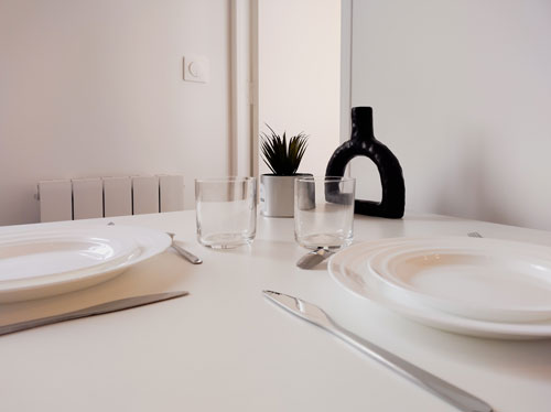 Table à manger avec une vaisselle blanche, un petit pot de plante grasse et un vase design en argile noire