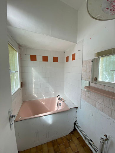 Salle de bain à rénover avec un biagnoire rose et du carrelage blanc