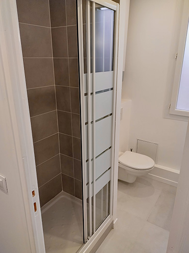 Salle de bain moderne et lumineuse avec un cabine de douche qui s'ouvre grâce à un système de porte coulissante, des WC suspendus et un meuble vasque avec des tiroirs de rangement