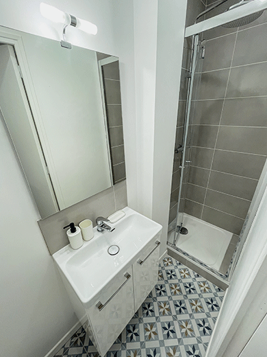 Belle salle de bain moderne et lumineuse avec de la crédence gris, un meuble vasque et un grand miroir, une cabine de douche très pratique et recherché par les futurs locataires
