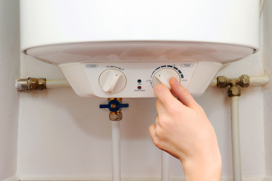 Une personne tourne le thermostat d'un ballon d'eau chaude