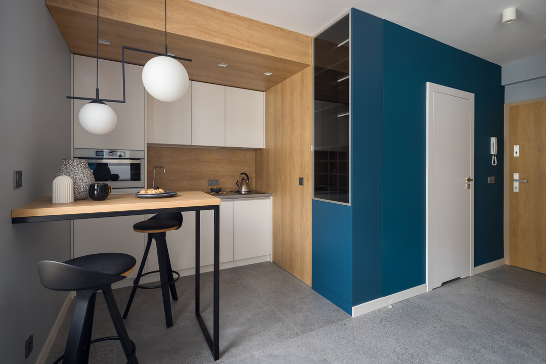 Vue sur la cuisine d'un appartement rénové avec des touches de bois de bouleau clair et des pans de murs peint en bleu