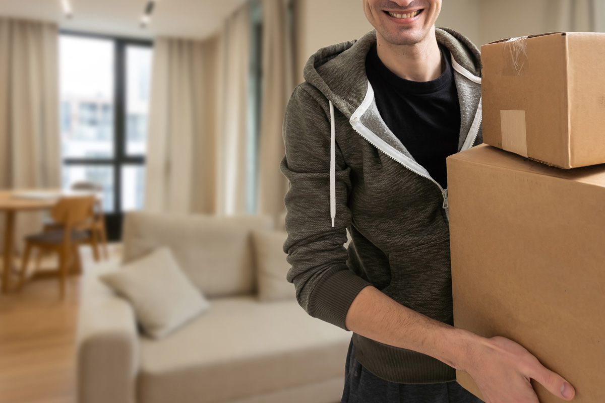 Un homme souriant transporte des boîtes de déménagement en carton.