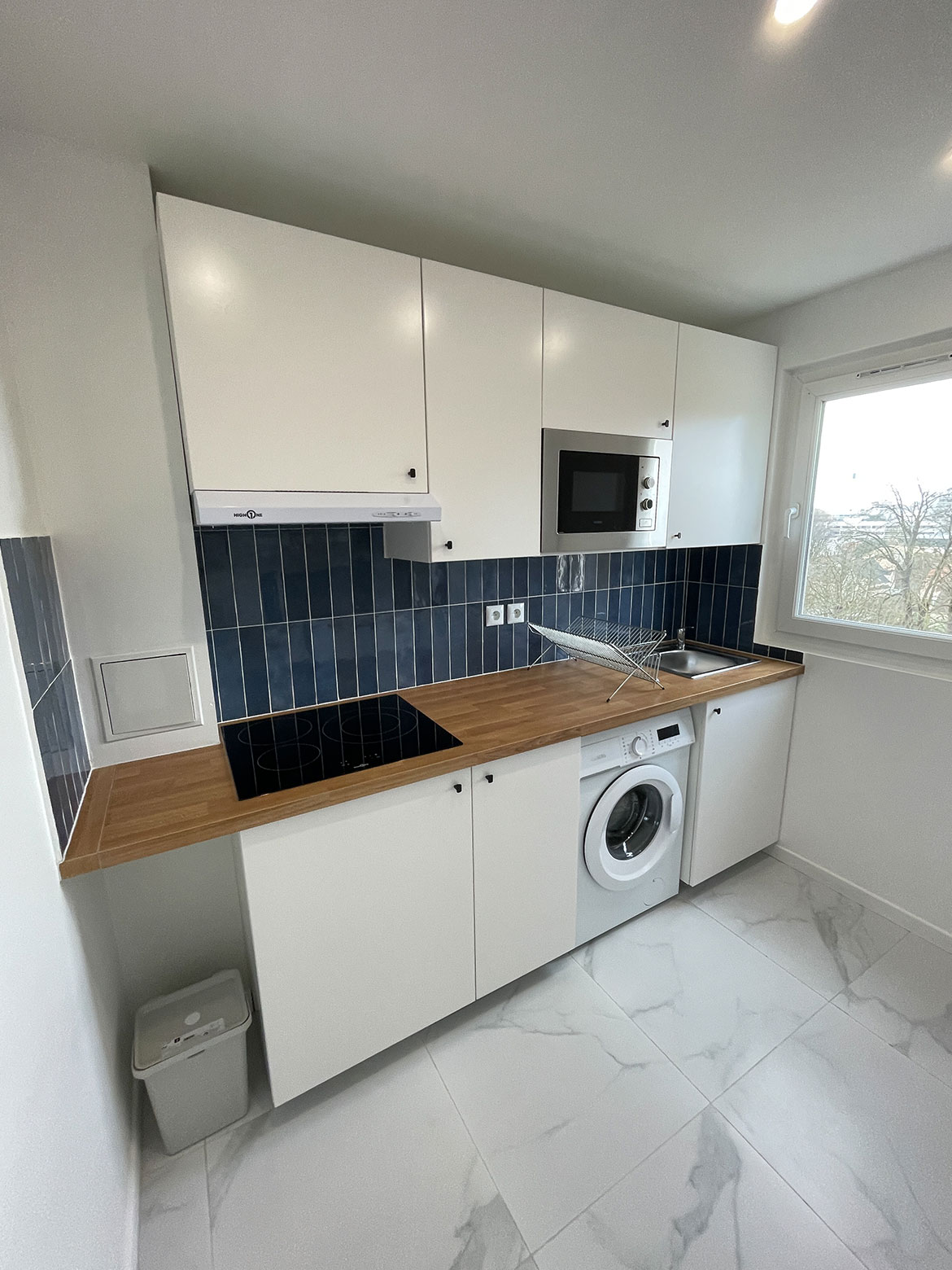 Cuisine après les travaux de rénovation avec un sol en imitation marbre et une crédence bleu imitant le zellige